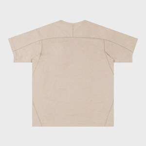 May include: A beige short-sleeved t-shirt with visible stitching details. The shirt has a crew neck and a relaxed fit. The seams are reinforced with a contrasting thread, adding a subtle design element. The fabric appears lightweight and breathable.