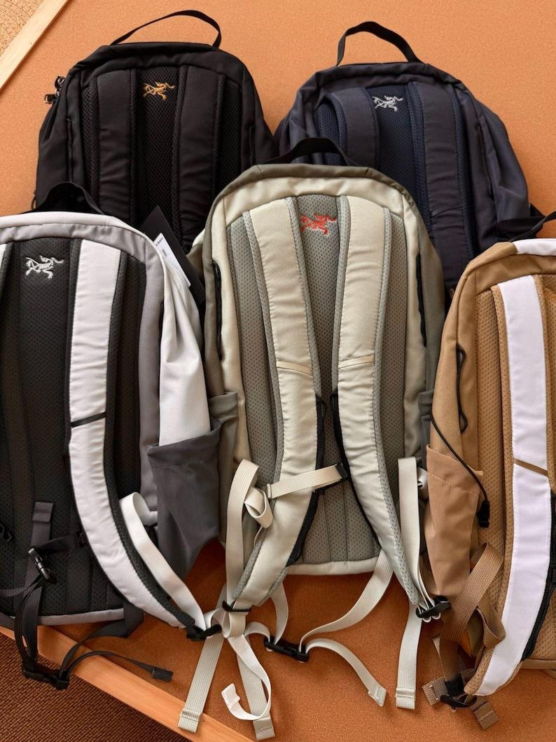 May include: A collection of backpacks in various colors, including black, navy, gray, and tan. Each backpack features a padded back panel, adjustable straps, and a logo. The backpacks are designed for outdoor activities and travel.