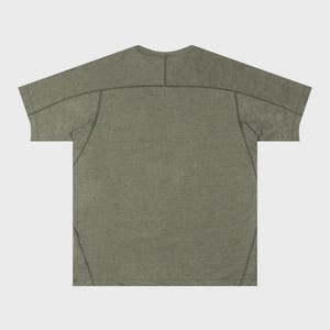 May include: Olive green t-shirt with a crew neck and short sleeves. The shirt has a textured appearance and features visible stitching details along the shoulders and sleeves. The back of the shirt is visible.