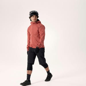 Puede incluir: Una persona con una chaqueta con capucha de color coral, pantalones cortos negros, guantes y zapatos, con un casco negro. El atuendo incluye rodilleras negras y calcetines estampados. La persona camina sobre un fondo blanco.