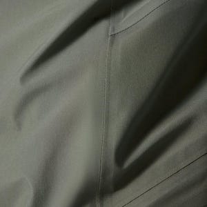 Puede incluir: Primer plano de tela verde oliva con textura y costuras visibles. La tela parece ser un material duradero, posiblemente impermeable, con sutiles variaciones de tono. La imagen sugiere una prenda de vestir o equipo para exteriores.