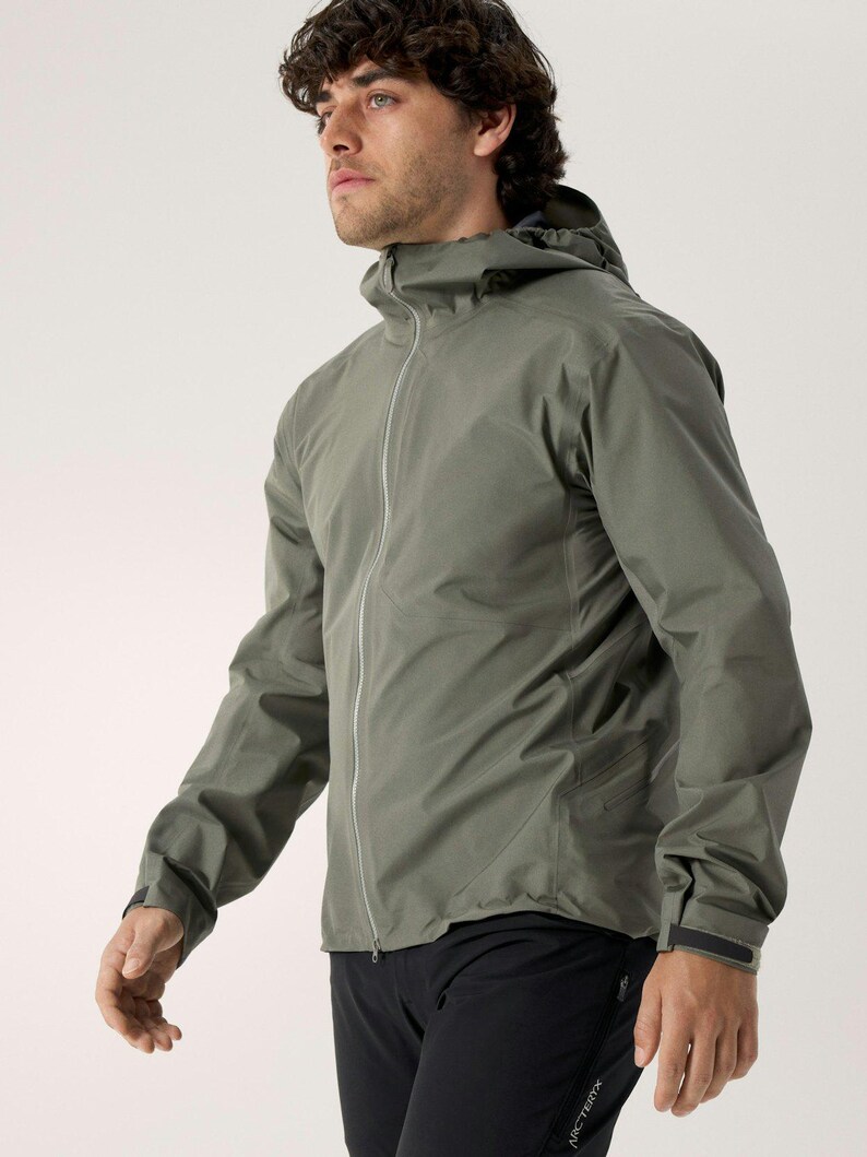 Puede incluir: Chaqueta con capucha verde salvia con cremallera completa. La chaqueta tiene un dise&ntilde;o aerodin&aacute;mico con una silueta ajustada y un brillo sutil. Las mangas tienen pu&ntilde;os ajustables. El modelo lleva pantalones deportivos negros.