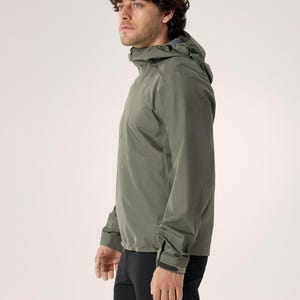 Puede incluir: Chaqueta con capucha verde oliva con mangas largas y cierre de cremallera. El modelo lleva pantalones negros. El modelo est&aacute; de perfil, mostrando el dise&ntilde;o de la chaqueta. Dise&ntilde;o minimalista.