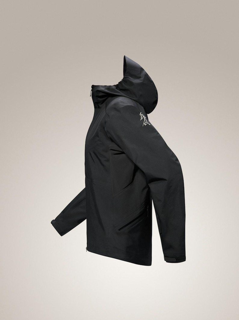 Puede incluir: Chaqueta negra con capucha, cierre de cremallera y peque&ntilde;o logotipo en la manga. La chaqueta tiene un dise&ntilde;o elegante y minimalista, adecuada para actividades al aire libre. La chaqueta est&aacute; hecha de un material ligero y resistente al agua.
