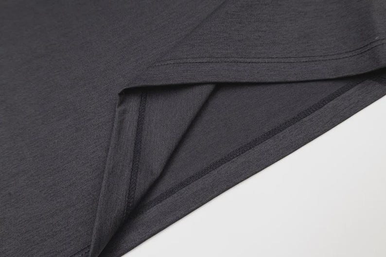 May include: Close-up of a dark gray t-shirt, showcasing the neckline and a portion of the fabric. The stitching is visible along the seams, highlighting the garment's construction. The fabric has a subtle texture.