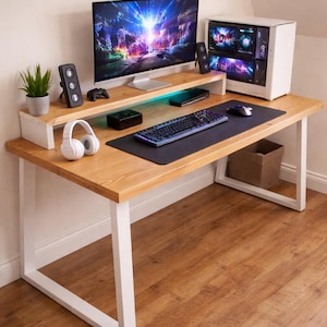 Peut inclure: Un bureau de jeu moderne avec un plateau en bois clair et des pieds en métal blanc. Le bureau comprend un écran, des haut-parleurs, un clavier, une souris et une unité centrale. Un casque et une petite plante sont également présents.