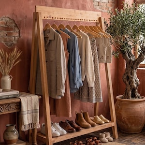 Puede incluir: Un perchero de madera exhibe varias prendas en perchas, incluyendo camisas y vestidos. Debajo, zapatos de diferentes estilos y colores están colocados en un estante. La escena está ambientada en una habitación con una estética rústica y terrosa.