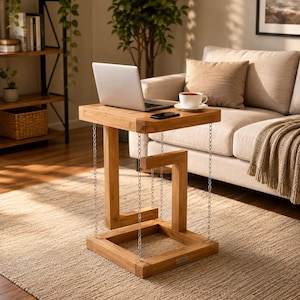 May include: A light brown wooden side table featuring a floating design supported by thin metal chains. The table has a square top and a square base connected by a central Z-shaped wooden structure, with a laptop and a coffee cup on the surface.