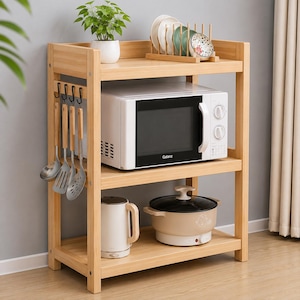 Puede incluir: Un estante de cocina de tres niveles de madera clara que cuenta con un microondas blanco en el estante central, un hervidor eléctrico blanco y una olla beige en el estante inferior, y un escurridor de platos de madera con platos arriba.