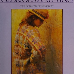 May include: Book cover featuring the title "GLORIOUS KNITTING" by Kaffe Fassett. The image shows a person wearing a colorful, patterned sweater and a straw hat. The book cover has a purple border and the text "OVER 30 EXCLUSIVE PATTERNS."