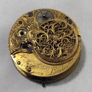 May include: Close-up of a vintage gold pocket watch movement. The intricate mechanism features ornate filigree and engraved details. The watch is marked "N. Hopkins London" and "2839". The overall design is a testament to craftsmanship.
