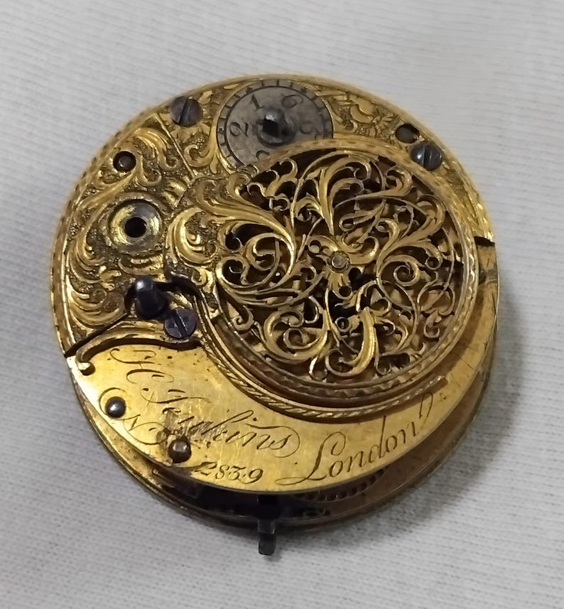 May include: Close-up of a vintage gold pocket watch movement. The intricate mechanism features ornate filigree and engraved details. The watch is marked "N. Hopkins London" and "2839". The overall design is a testament to craftsmanship.