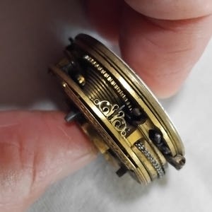 May include: Close-up of a vintage pocket watch mechanism. The intricate gold-toned gears, springs, and decorative elements are visible. The watch is partially open, revealing the internal workings and craftsmanship of the antique timepiece.