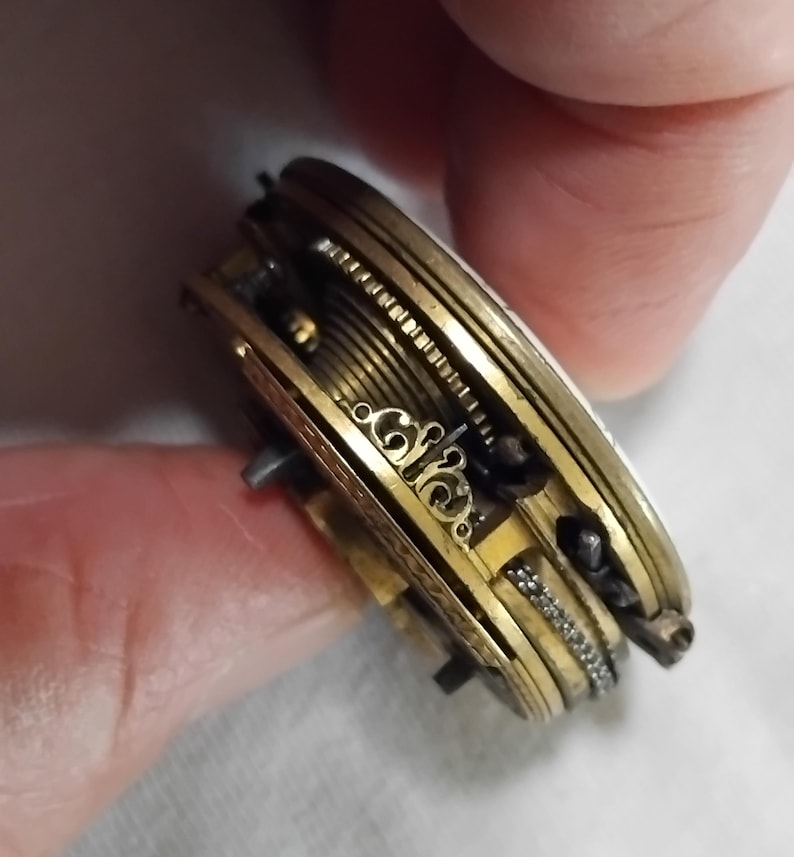 May include: Close-up of a vintage pocket watch mechanism. The intricate gold-toned gears, springs, and decorative elements are visible. The watch is partially open, revealing the internal workings and craftsmanship of the antique timepiece.