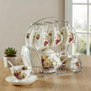 Peut inclure: Un service à thé composé d'une théière, d'un pot à lait et de plusieurs tasses et soucoupes en porcelaine blanche ornées de motifs floraux colorés. L'ensemble est disposé sur un support en métal chromé avec une anse incurvée.