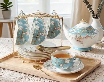 May include: A tea set featuring a light blue porcelain teapot, cups, and saucers decorated with white and pink almond blossom patterns. The set includes a gold-toned metal rack for holding cups and saucers, along with small gold-toned spoons.