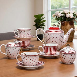 Può includere: Un set da tè in ceramica con base bianca, pois rossi e strisce verticali rosse. Il set comprende una teiera con coperchio rosso, una lattiera, una zuccheriera con coperchio e diverse tazze con piattini abbinati, rifinite con dettagli dorati.