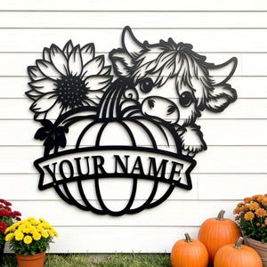 Puede incluir: Letrero de metal negro con una vaca asomándose por encima de una calabaza, con un girasol y el texto "YOUR NAME". El letrero se exhibe al aire libre con calabazas y flores en macetas.