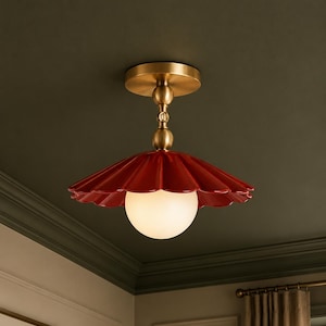 May include: A red, scalloped-edge ceiling light fixture with a brass-colored stem and ceiling mount. The light has a white, spherical bulb. The fixture is mounted on a dark green ceiling.