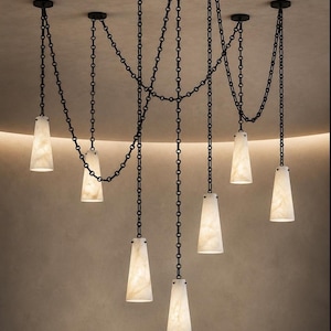 Può includere: Un lampadario a sospensione multipla con sette paralumi conici in pietra bianca traslucida, appesi al soffitto tramite catene in metallo nero. Le catene sono disposte a festone, collegando ogni punto luce a fissaggi a soffitto individuali.