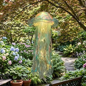 May include: A hanging jellyfish-shaped garden ornament. The translucent, iridescent material catches the light, creating a shimmering effect. The ornament is suspended from a tree branch in a lush garden setting, with colorful flowers and greenery in the background.