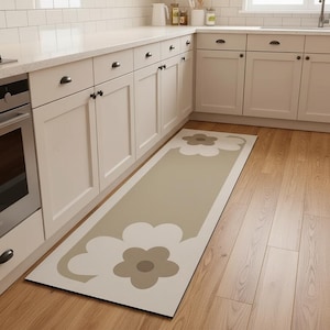 Könnte beinhalten: Ein rechteckiger Küchenteppich mit floralem Design. Der Teppich hat eine beige Mittelbahn mit großen, stilisierten Blumenformen in Weiß und Taupe. Der Teppich liegt vor weißen Schränken und einem Holzboden.