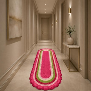 May include: An oval-shaped crochet runner rug featuring concentric bands of vibrant hot pink, light green, and cream yarn. The rug has a decorative scalloped edge border in hot pink, creating a textured finish throughout the entire piece.