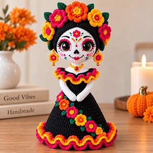 May include: A crocheted doll featuring a white face with black and red sugar skull makeup, large brown eyes, and a black hair crown adorned with vibrant orange, yellow, and pink flowers. The doll wears a black dress with a ruffled neckline and hem.