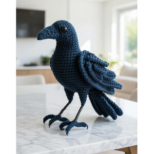 Könnte beinhalten: Handgefertigte, dunkelblaue Häkel-Raben-Skulptur. Der Vogel hat einen detaillierten Schnabel, Knopfaugen und strukturierte Flügel. Seine Beine sind aus Draht gefertigt und er steht auf einer marmorierten Oberfläche. Ein dekorativer Artikel.
