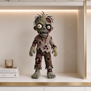 May include: A crocheted zombie doll with light green skin, messy black yarn hair, and large white eyes with black pupils. It wears a tattered beige shirt and brown pants, both featuring red yarn accents to simulate blood stains and holes.