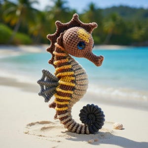 Puede incluir: Un caballito de mar de ganchillo hecho a mano en tonos marrón, beige, amarillo y gris, con ojos azules. El caballito de mar está sobre una playa de arena con el océano al fondo. El caballito de mar mide unos 20 cm de alto.