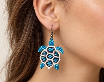 May include: A dangle earring shaped like a sea turtle, crafted from small beads in shades of bright turquoise, white, and black. The turtle figure features a geometric shell pattern and is suspended from a dark metal hook-style earring wire.