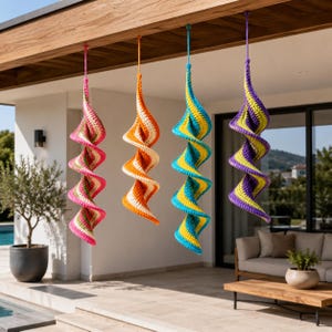 May include: Four spiral crochet ornaments in vibrant colours suspended from a wooden beam. The ornaments feature pink, orange, blue, and purple with white accents. The crochet work creates a textured, decorative effect, suitable for indoor or outdoor decoration.