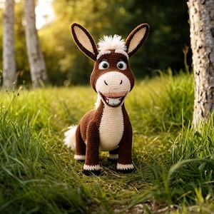 May include: A handmade crochet donkey toy with brown and white yarn. The donkey has large ears, a white muzzle, and a smiling expression. It is standing in a grassy area with trees in the background.