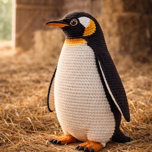 Peut inclure: Un pingouin crochet&eacute; &agrave; la t&ecirc;te, au dos et aux ailes noirs, au ventre blanc et aux pieds et au bec orange. Il se tient sur de la paille. L'arri&egrave;re-plan montre une structure en bois et des balles de foin.