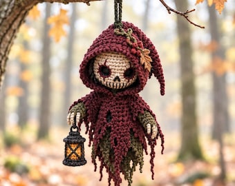 May include: A crocheted doll featuring a skull-like face with dark eye sockets, wearing a hooded burgundy cloak with frayed edges and a small leaf accent. The doll has olive green sleeves, claw-like hands, and holds a small black lantern with a glowing orange light.