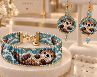 May include: A beaded bracelet and a pair of matching drop earrings featuring a brown and cream otter design on a blue background with white waves. The jewelry set includes gold-toned hardware, a paw print charm, and small blue crystal accents.