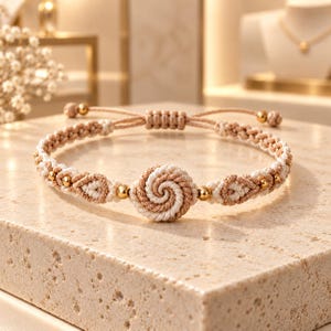 May include: A macrame bracelet featuring a central spiral knot in beige and cream cord, accented with small gold-toned metallic beads. The band is constructed from braided cord with adjustable sliding knots at the back, showcasing a symmetrical design.