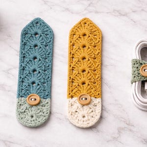 May include: Crocheted cable organizers in blue, yellow, and green with wooden button closures. The blue and yellow organizers have a decorative pattern, while the green one wraps around a white cable.