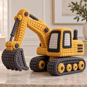 May include: A crocheted toy excavator in yellow and dark gray yarn. The construction vehicle features a movable boom arm, a large dark gray bucket, a cab with white windows, and tracked wheels with yellow circular accents on the sides.