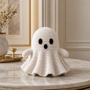 May include: A white crochet ghost figurine featuring a rounded head, two small black oval eyes, and a small black oval mouth. The body of the ghost is textured with visible yarn stitches and flares out at the bottom into a ruffled, skirt-like shape.