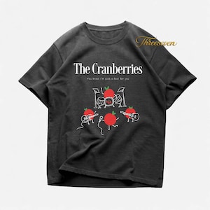 May include: Charcoal grey t-shirt with the band name "The Cranberries" in white, and the phrase "You know I'm such a fool for you". The graphic depicts red anthropomorphic cranberries playing drums and guitars, a fun design.