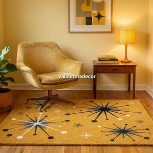 Op de afbeelding: Mosterdgeel tapijt met een mid-century modern sterrenpatroon. Het tapijt ligt in een kamer met een gele stoel, een bijzettafel en een lamp. Een plant in een pot staat in de hoek. Het ontwerp van het tapijt heeft zwarte, witte en grijze sterren.
