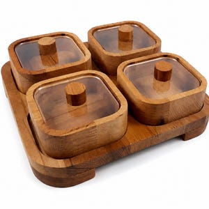 May include: A square wooden serving tray featuring four individual square wooden containers. Each container has a clear, transparent lid with a small, centered wooden knob handle. The natural wood grain is visible throughout the entire set.