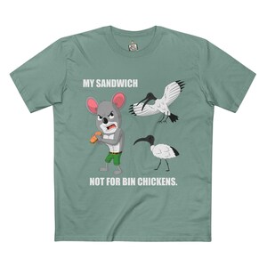 May include: Sage green t-shirt with a cartoon graphic. The graphic shows an angry mouse holding a sandwich, with the text "MY SANDWICH NOT FOR BIN CHICKENS." Two black and white birds are also depicted.