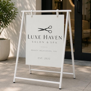 May include: A white A-frame pavement sign featuring a black scissor icon and the text Luxe Haven Salon & Spa, Beauty, Relaxation, You, Est. 2022. The sign is constructed with a sturdy metal frame and a rectangular display panel for business signage.