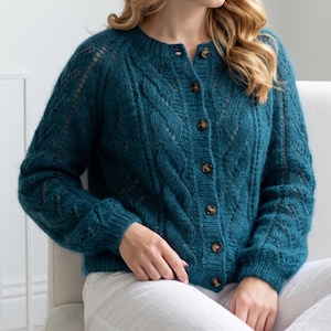 May include: Teal-colored knitted cardigan with a button-up front. The cardigan features a cable knit design on the front and sleeves, with a round neckline and wooden buttons. The sleeves are long and the cardigan is made of a soft, textured yarn.