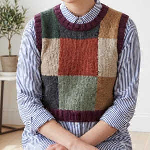 Könnte beinhalten: Eine Patchwork-Strickweste in verschiedenen Farben, darunter Grün, Beige, Rot und Grau. Die Weste hat einen gerippten bordeauxfarbenen Ausschnitt und Saum. Sie wird über einem blau-weiß gestreiften Button-Down-Hemd getragen.