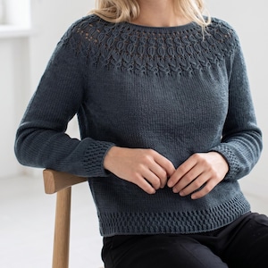 May include: A dark teal long-sleeve sweater featuring a round neckline with an intricate leaf-like lace pattern across the yoke. The garment includes ribbed cuffs and a matching ribbed hem, showcasing a consistent knit texture throughout the body.