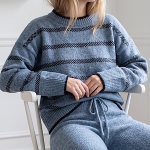 May include: A light blue knit jumper and matching trousers set featuring horizontal black stripes. The jumper has a crew neckline with black trim, long sleeves with ribbed cuffs, and a ribbed hem. The trousers feature an adjustable drawstring waist.